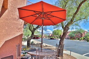 An outdoor seating area with a red umbrella, metal chairs, and a table.