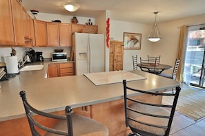 A kitchen with wooden cabinets, a refrigerator, a microwave, a dining table with chairs, and a hanging light fixture.