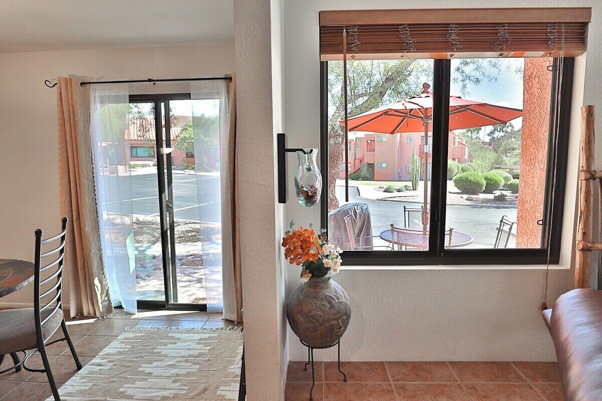 A room with a sliding glass door leading outside, a dining area with a table and chairs, and a window with a view of the outside.
