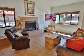 A living room with a fireplace, a reclining chair, a television, and a window with blinds.