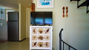 Una cocina con refrigerador, un televisor sobre un mueble y una escalera.