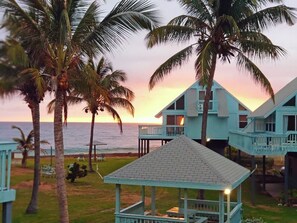 Una propiedad frente a la playa con varios edificios azules, un pabellón y palmeras.