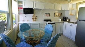 Una cocina compacta con armarios blancos, una mesa de comedor de superficie de vidrio y sillas azules.