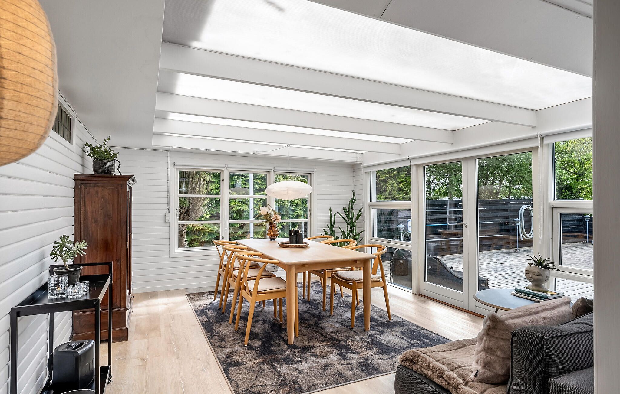 Una habitación luminosa e inundada de luz, con una mesa y sillas de madera, ventanas amplias y vistas al exterior.