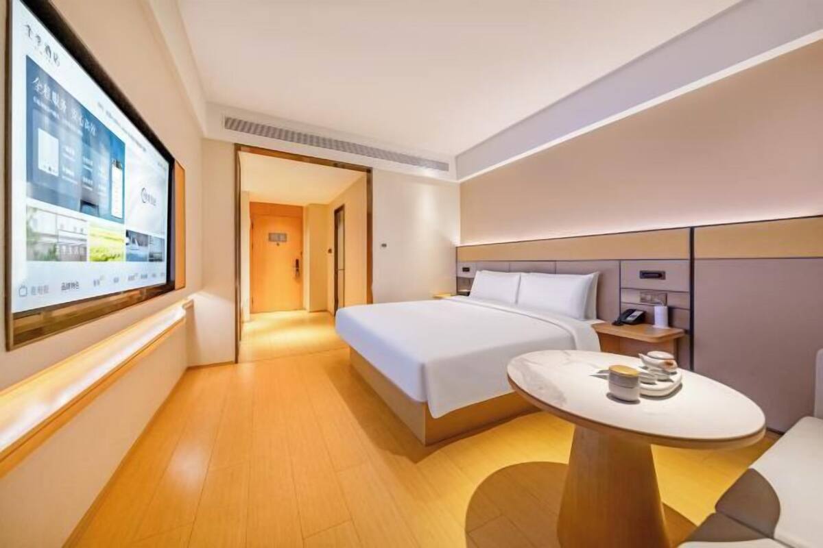 A modern hotel room with a large bed, bedside table, and a small round table with a lamp.