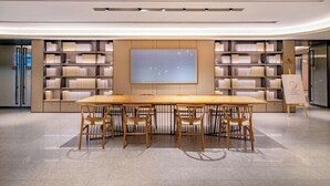A modern library with a long wooden table and chairs, surrounded by bookshelves.