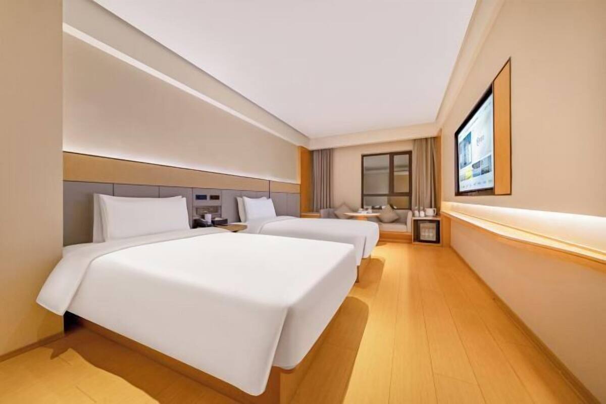 A hotel room with two beds, a TV, a desk, and a window.