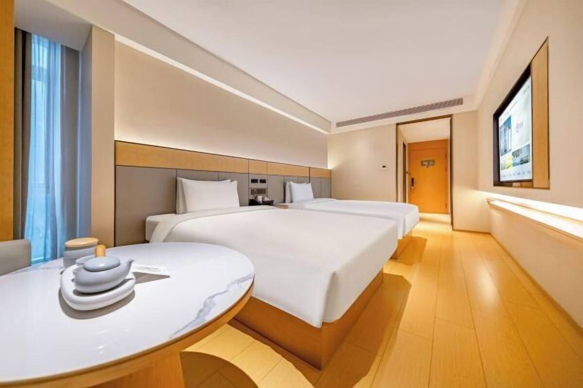 A modern hotel room with two beds, a round dining table, and a television mounted on the wall.
