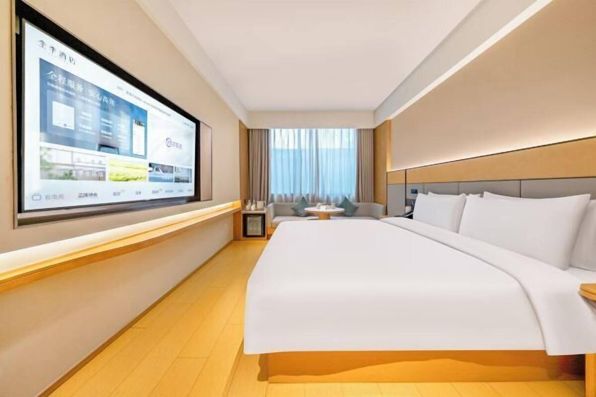 A hotel room with a large bed, a TV mounted on the wall, a sofa, and a small table.