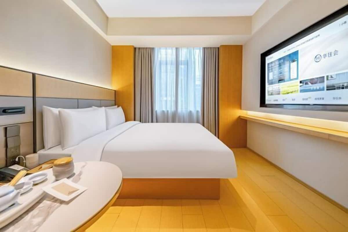 A modern hotel room with a large bed, a bedside table, a TV screen, and a window with curtains.