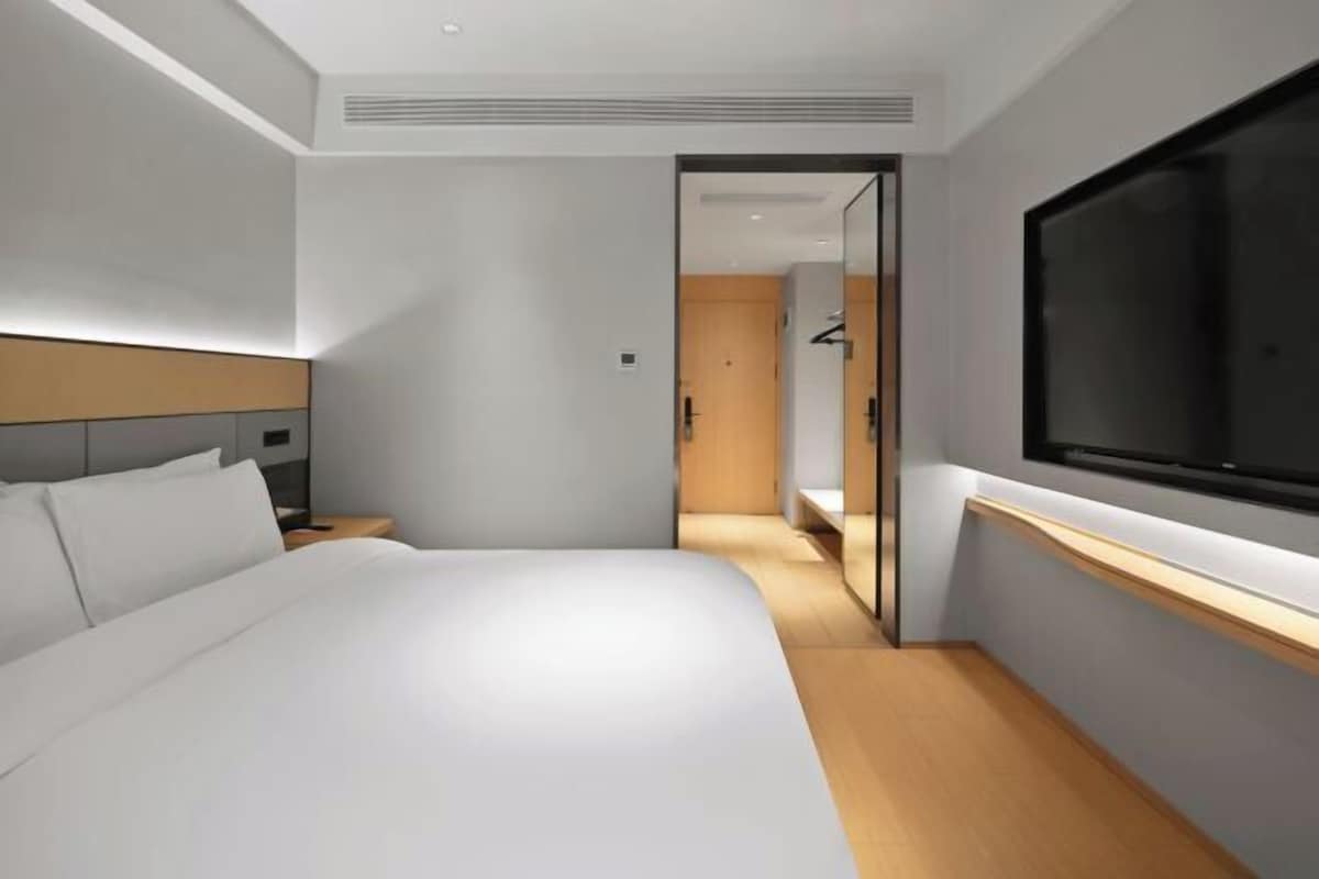 Quarto de hotel moderno com uma cama grande, televisão fixada na parede e piso de madeira.