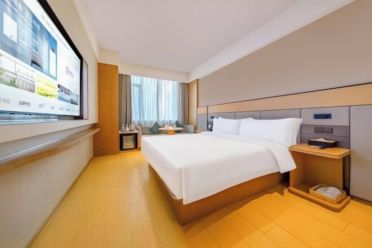 A hotel room with a bed, bedside table, and a TV screen displaying property listings.