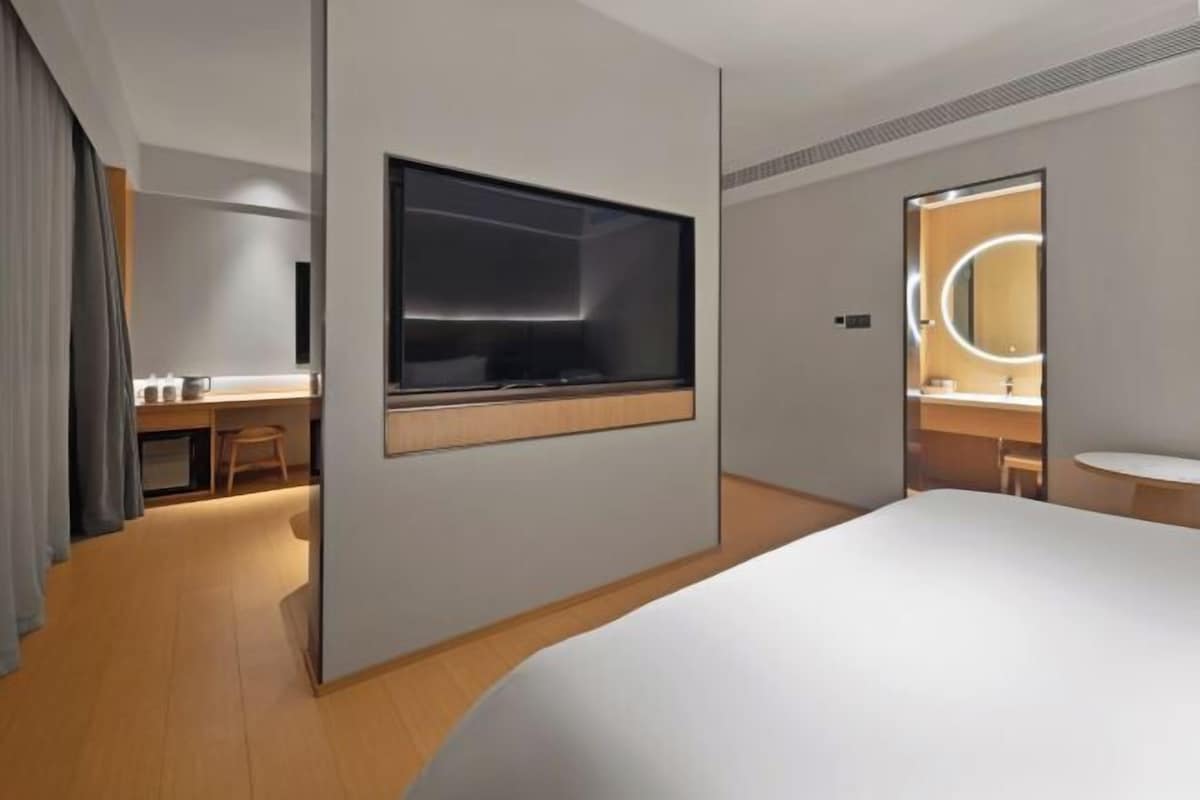 Quarto de hotel moderno com uma cama grande, uma escrivaninha com cadeira, uma televisão e um banheiro com espelho e iluminação.