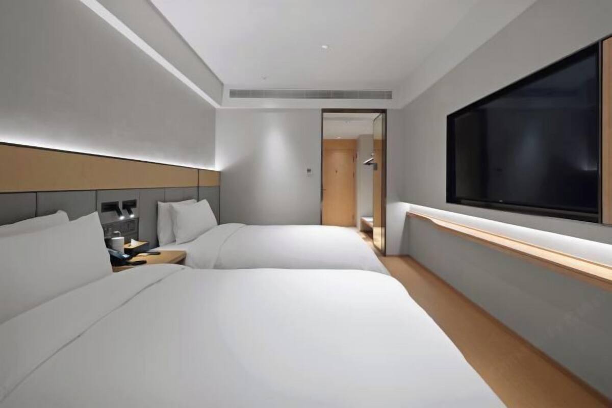 A modern hotel room with two beds, a large TV, and a walk-in closet.