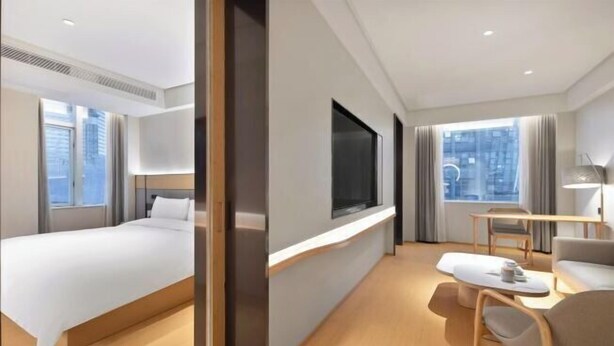 A modern hotel room with a bed, a desk, and a seating area.