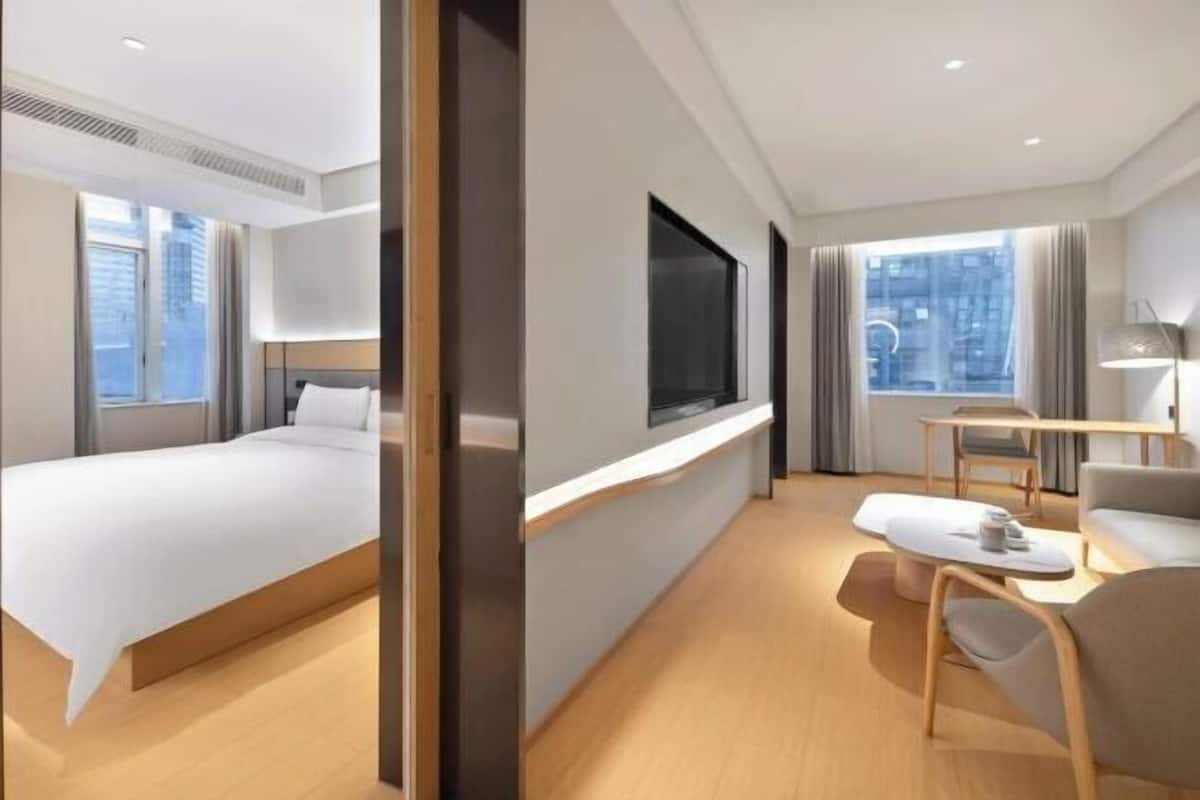 A modern hotel room with a bed, a desk, and a seating area.