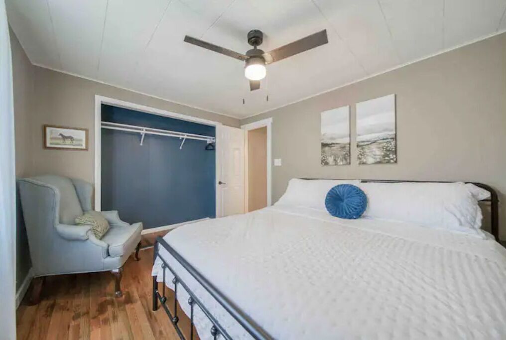 A bedroom with a bed, a chair, a ceiling fan, and a door leading to a closet.