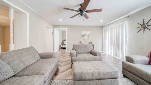 A spacious living room with a ceiling fan, a herringbone-patterned floor, and a large window with sheer curtains. - Vineyard Ridge Farmhouse • 3BR • 2BA • Vineyard View • Fire pit • 
 (Saint James)