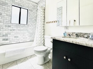 A bathroom with a white toilet, a bathtub, a shower curtain, a marble countertop, and a black cabinet.