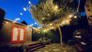 Un patio con un árbol, luces colgantes y un edificio con puertas rojas.