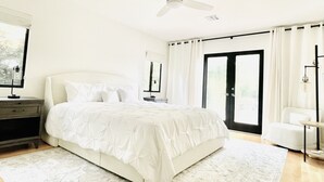 Un dormitorio con una cama grande, una mesita de noche, una silla y vistas al exterior a través de una puerta corrediza.