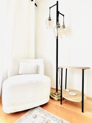 A modern bedroom with a white sofa, a small round table, and a floor lamp with two clear glass shades.