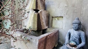 Una estatua de Buda sentada sobre una plataforma de piedra con un cuenco, junto a una estructura de piedra con una rama de árbol.