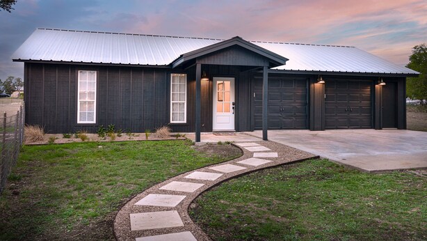 A modern two-story house with a dark exterior, a metal roof, and a front garage. - The Stargazer (Wimberley)