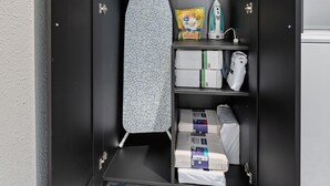 A compact storage unit with a hanging iron, a small ironing board, and neatly organized laundry and toiletries. - The Stargazer (Wimberley)