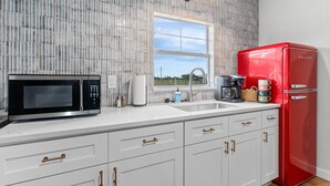 A kitchen with white cabinets, a red refrigerator, a microwave, and a window with a view of the outdoors. - The Stargazer (Wimberley)