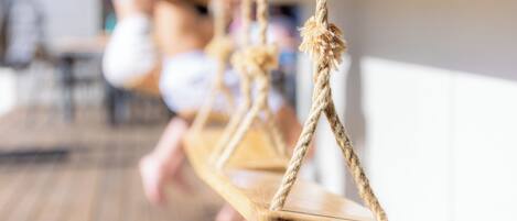 A wooden swing suspended by ropes in a room with a wooden floor.
