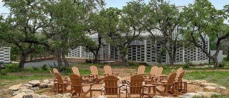 Un espace circulaire aménagé avec des fauteuils Adirondack disposés autour d’un foyer, le tout entouré de rochers et d’arbres.