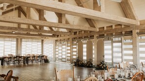 A spacious hall with wooden beams, large windows, and tables set for a formal event. - The Cedars Ranch (Wimberley)
