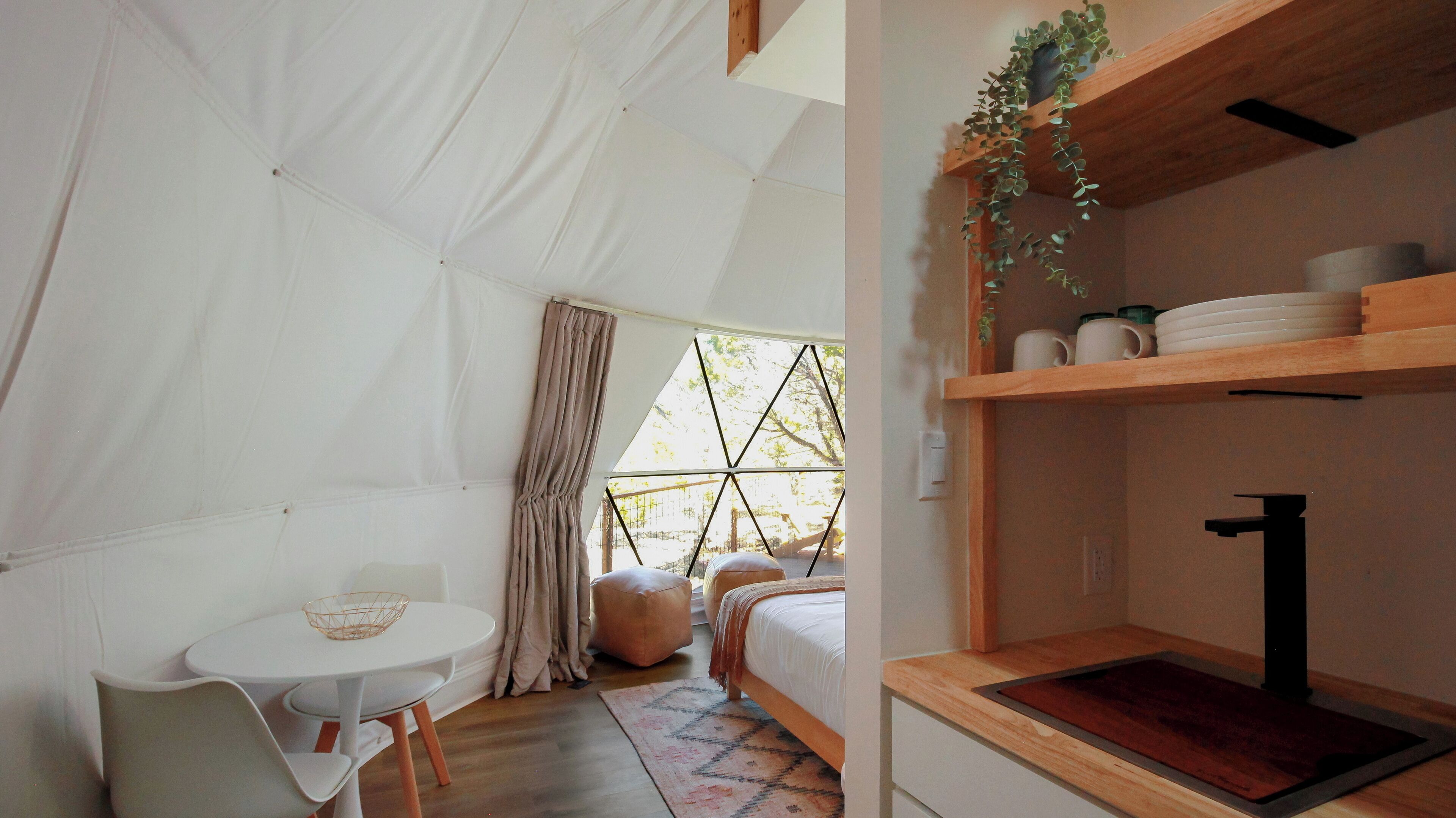 A tent-style room with a bed, a small table, and a shelf with kitchen items.