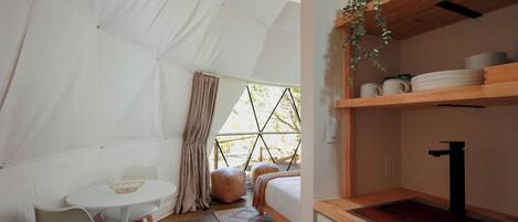 A tent-style room with a bed, a small table, and a shelf with kitchen items.