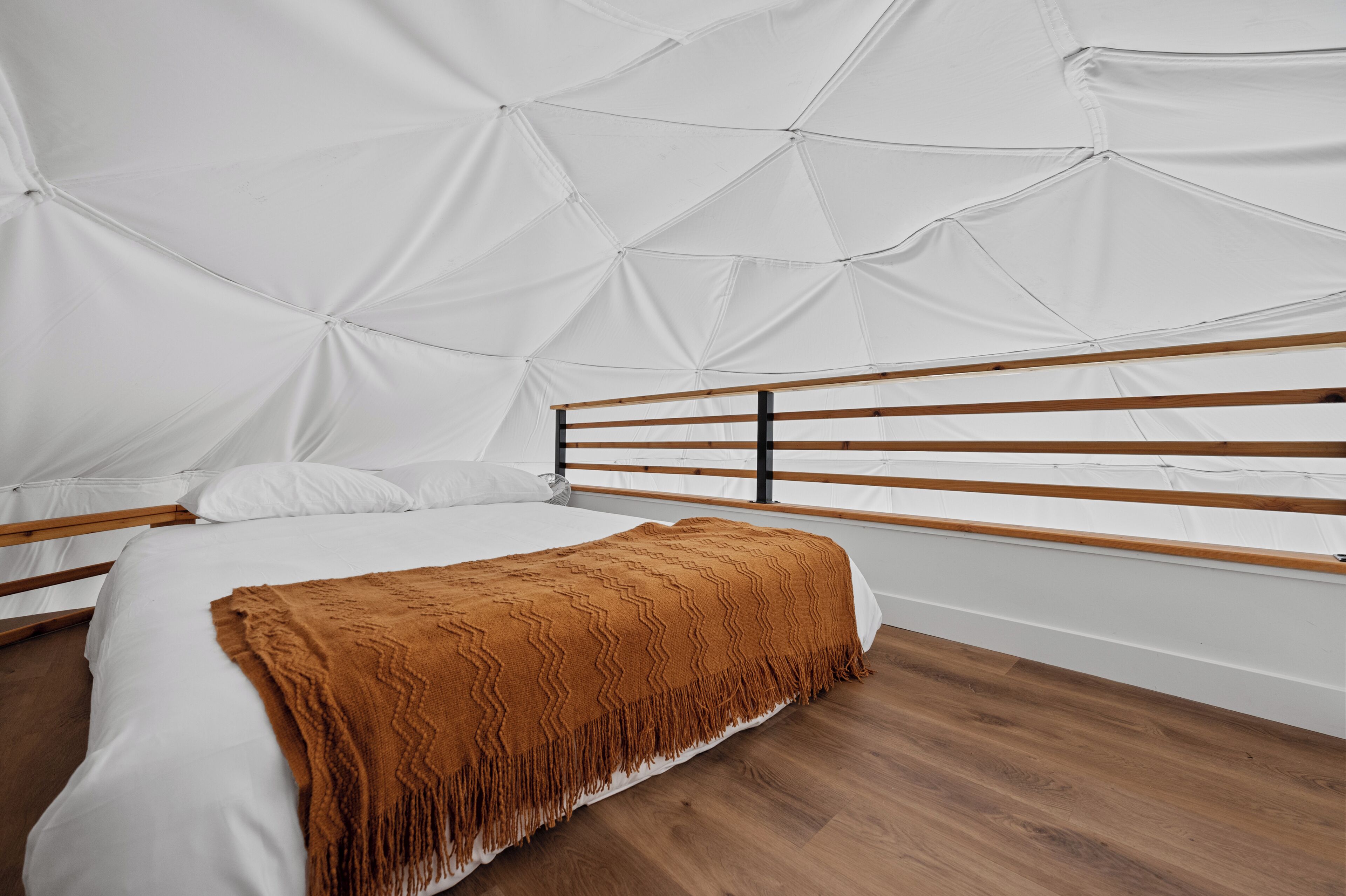 Un dormitorio moderno con un diseño geométrico en el techo, un cabecero de madera y una manta marrón.