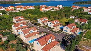 A coastal residential area with houses featuring red-tiled roofs and stone walls, surrounded by greenery and a clear view of the sea. - Gorgeous home in Pasman (Pasman)