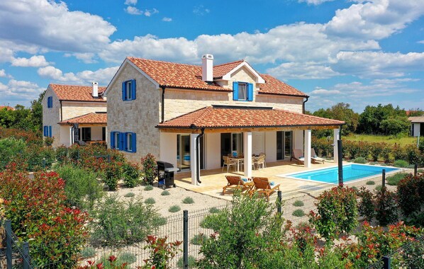 Une maison à deux étages avec une piscine, un espace salon extérieur et un jardin.