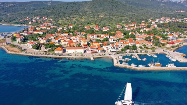 An aerial view of a coastal town with a marina, houses with red roofs, and a sailboat in the water. - Gorgeous home in Pasman (Pasman)