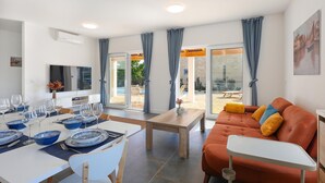 A modern living room with a sofa, a dining table set with blue bowls and wine glasses, and a TV on the wall. - Gorgeous home in Pasman (Pasman)