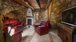 A stone-walled room with a fireplace, red leather sofas, a television, and a stone bench. - Beautiful home in Rasopasno with sauna (Rasopasno)