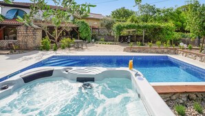 A swimming pool with a hot tub in the foreground, surrounded by a stone wall and lush greenery. - Beautiful home in Rasopasno with sauna (Rasopasno)