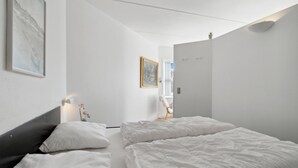 A modern hotel room with a large bed, a desk, and a chair. There is a painting on the wall and a window with a view.