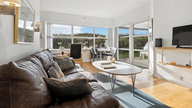 A modern living room with a leather sofa, a round coffee table, and a dining area with a table and chairs.