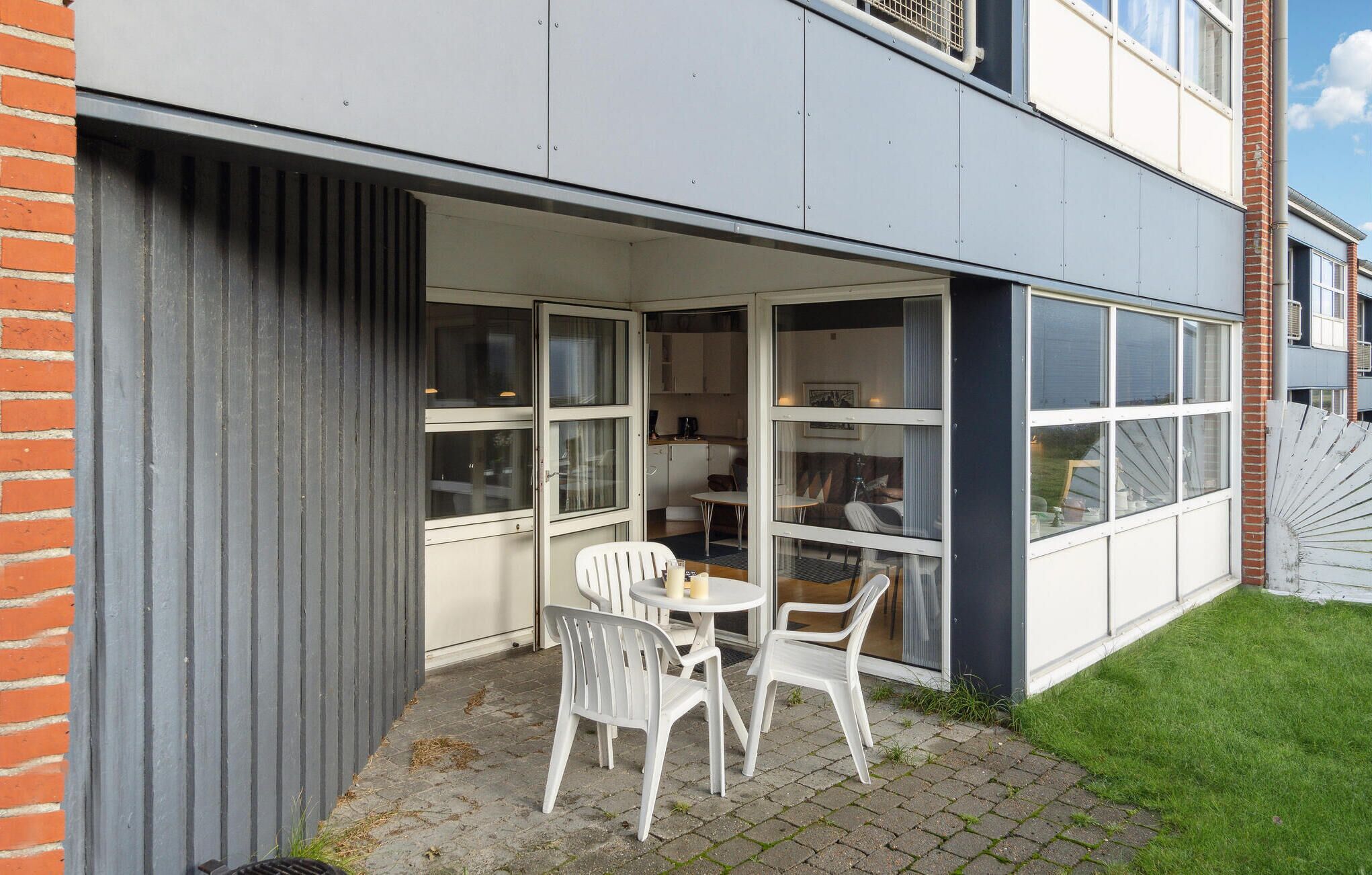 A modern building with a patio area featuring a table and chairs, large windows, and a brick wall.