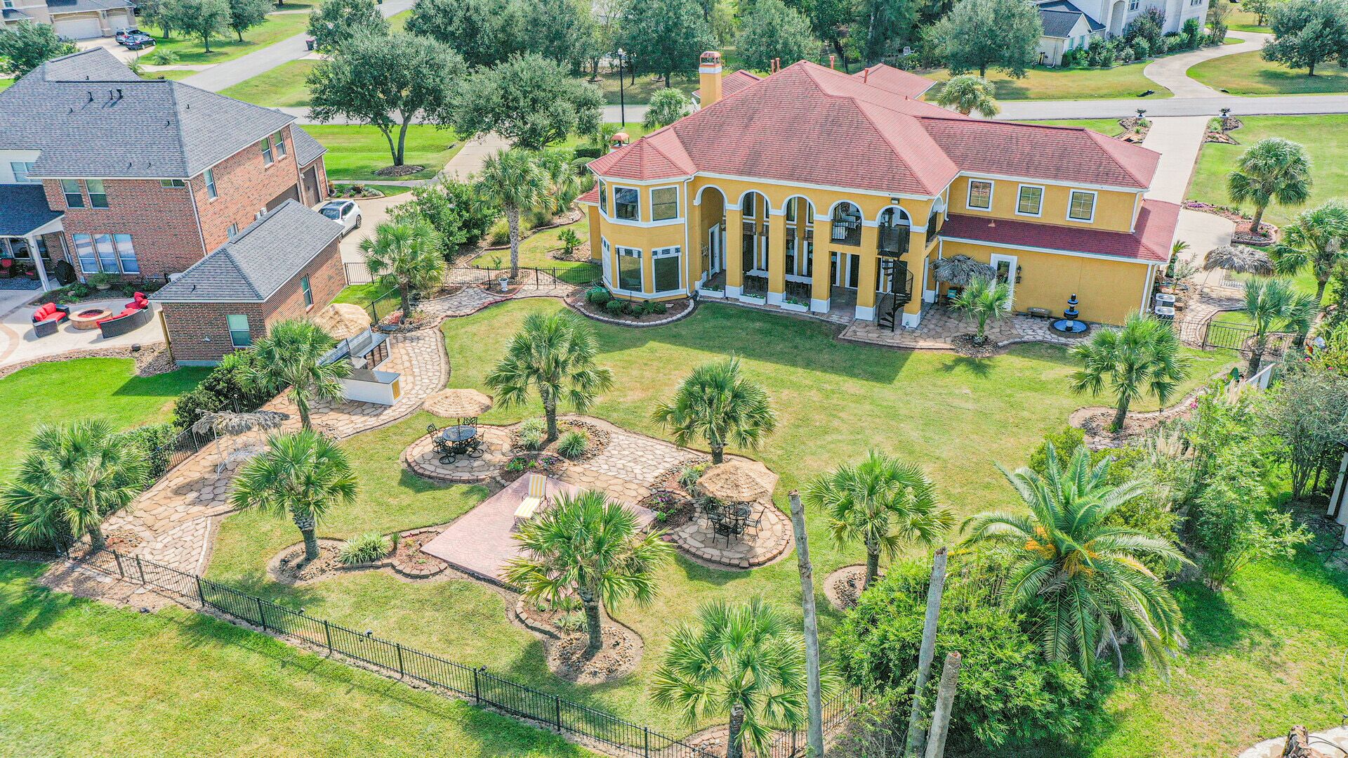 A large, yellow house with a red roof, surrounded by a well-maintained lawn and palm trees.