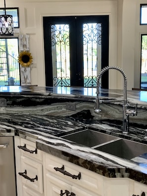 Een keuken met een zwart marmeren aanrecht, een roestvrijstalen spoelbak en een decoratieve metalen kraan.