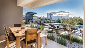 An outdoor patio area with a wooden table and chairs, a barbecue grill, lounge chairs, and a pool. - Awesome home in Vodnjan with private swimming pool, can be inside or outside (Vodnjan)