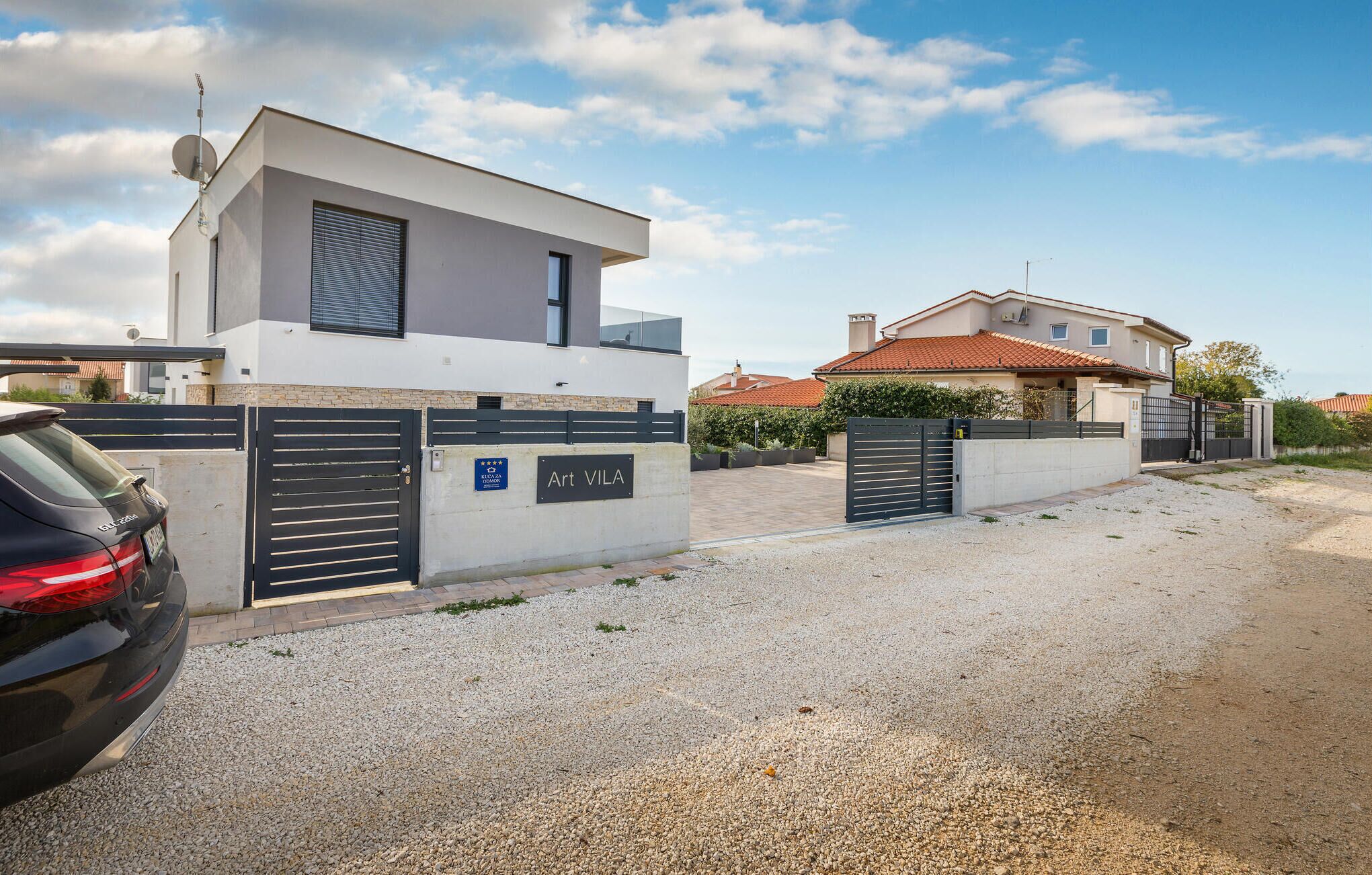 A modern two-story house with a gated entrance, a satellite dish, and a sign indicating 'Art Vila'.