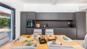 A modern kitchen with dark cabinetry, a built-in oven, and a large dining table set for breakfast. - Awesome home in Vodnjan with private swimming pool, can be inside or outside (Vodnjan)